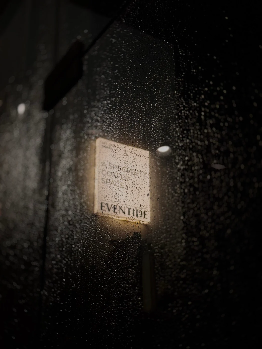 Rain droplets on glass with a softly lit sign beyond