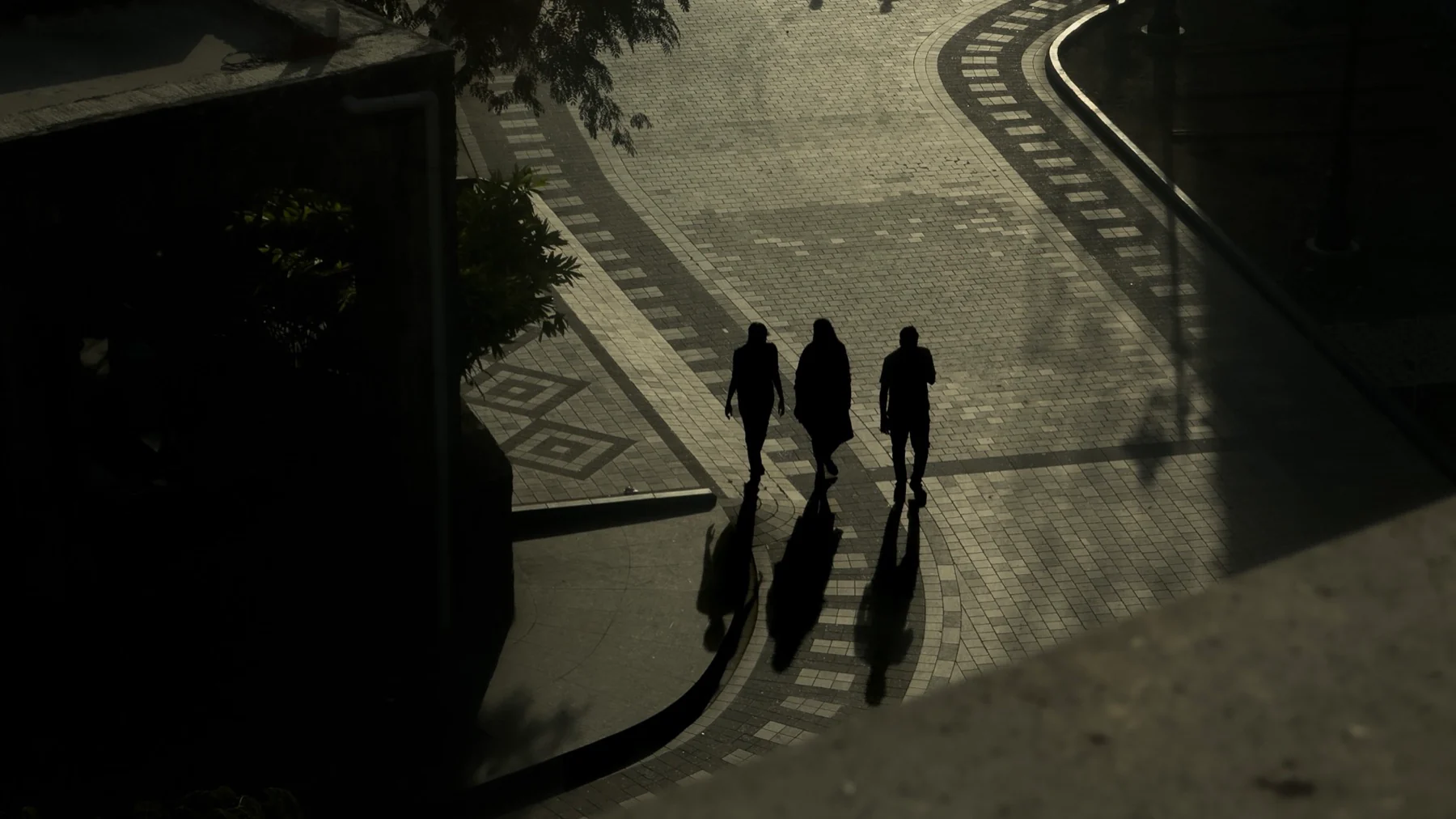 Three people and their long shadows crossing a patterned walkway